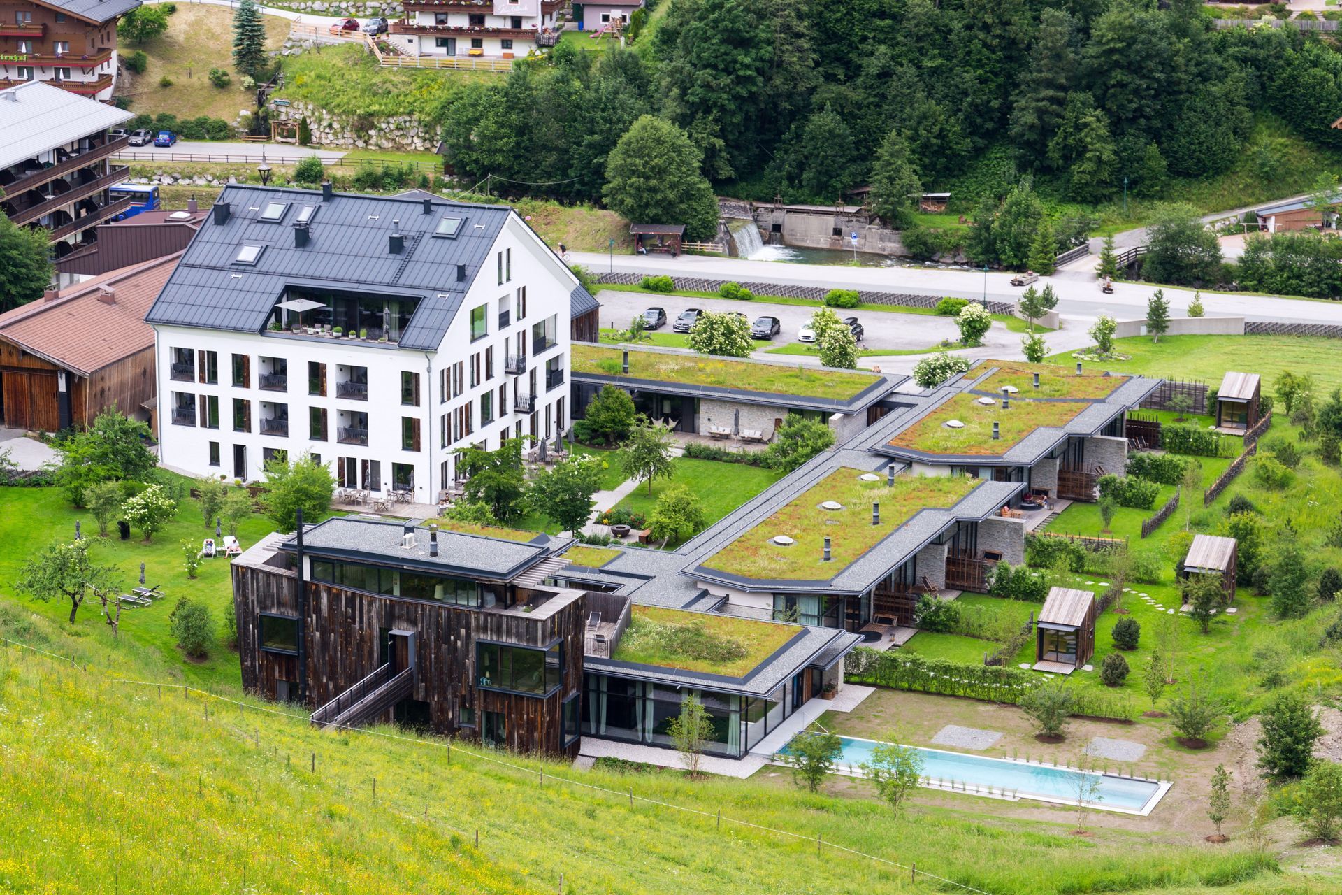 A modern resort with green roofs and a pool sits on a hillside with mountain views.