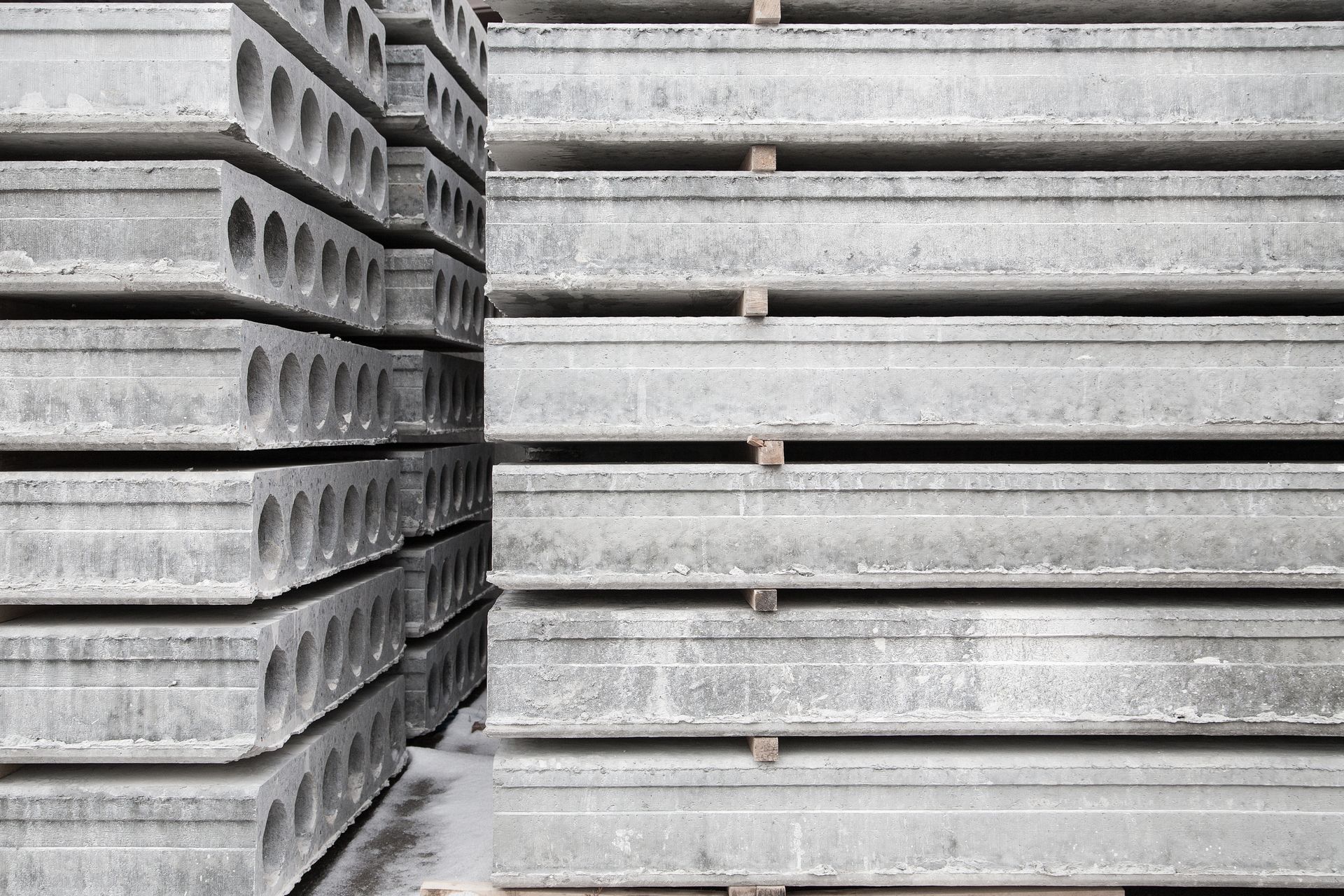 Stacks of precast concrete slabs, some with round holes, outdoors.