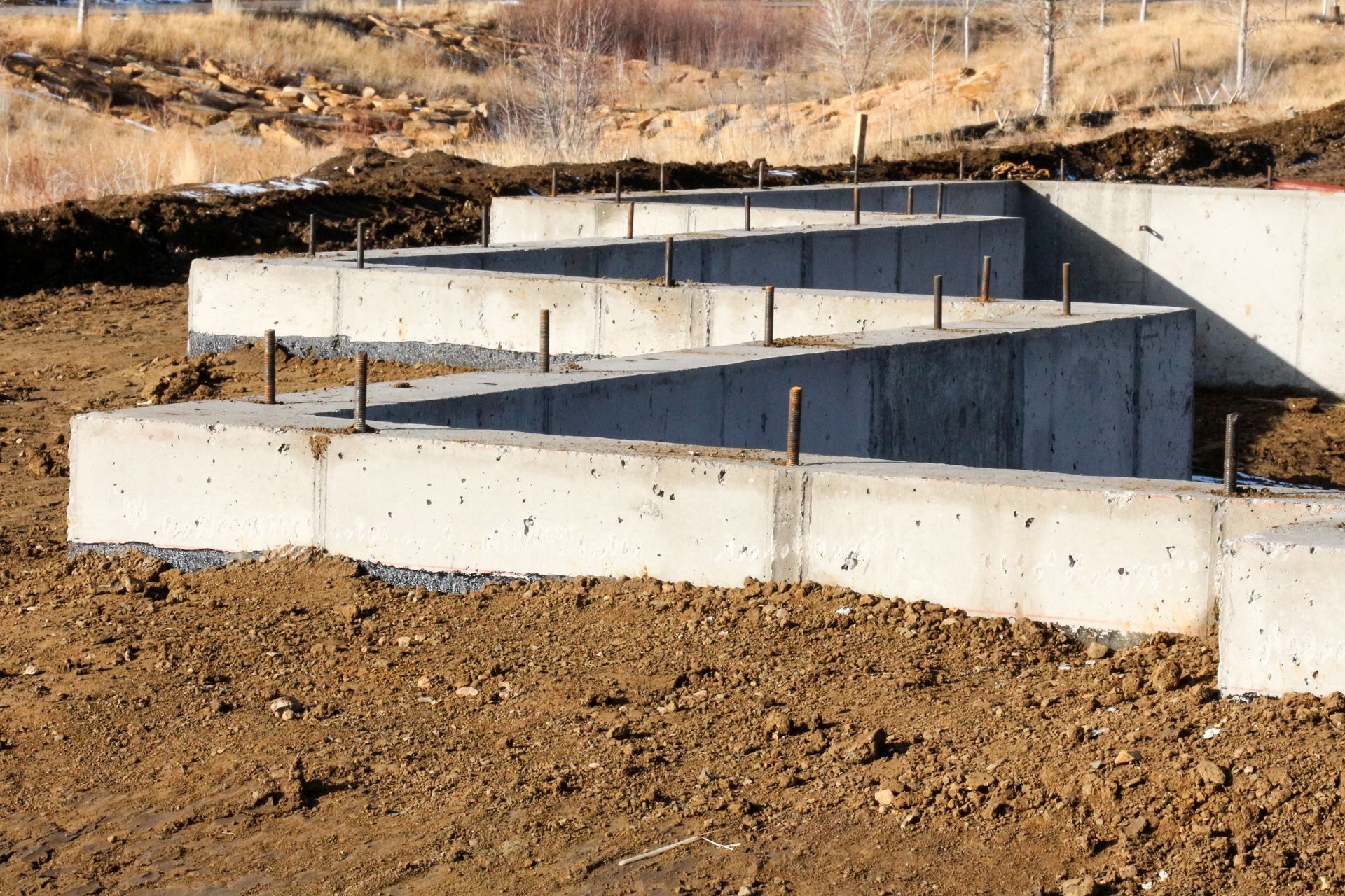 Concrete foundation walls with vertical anchor bolts installed at a construction site.