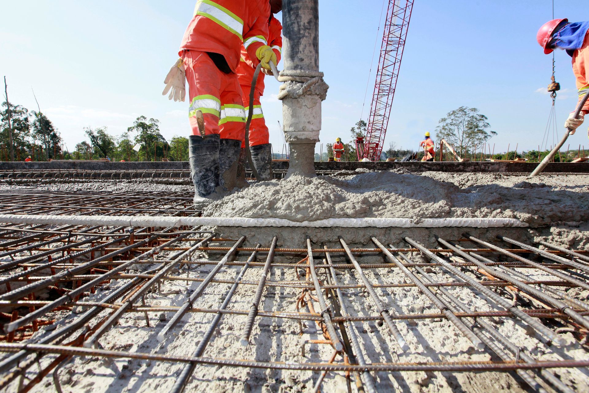 Workers in orange suits pouring concrete over rebar on a construction site.