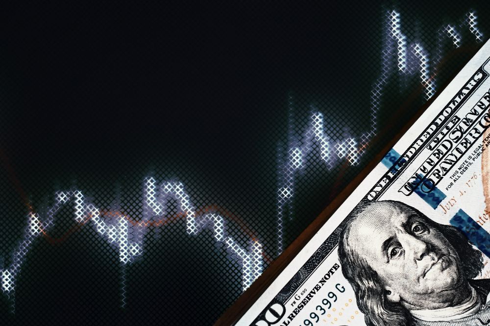 Nota de cem dólares cobrindo parcialmente um gráfico do mercado de ações, representando finanças e investimentos.