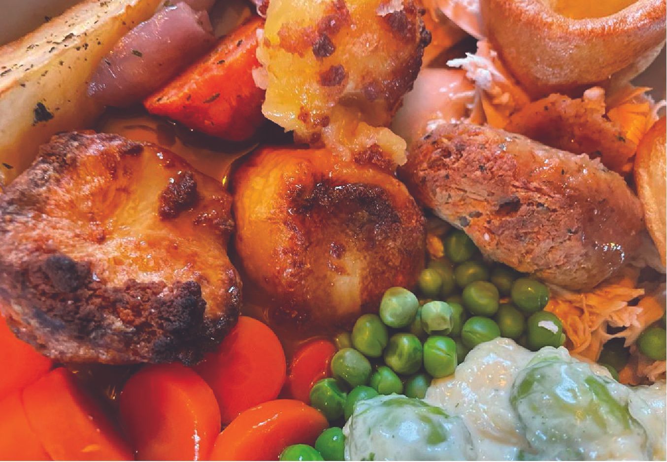 A close up of a roast dinner with meat , potatoes , carrots and peas.