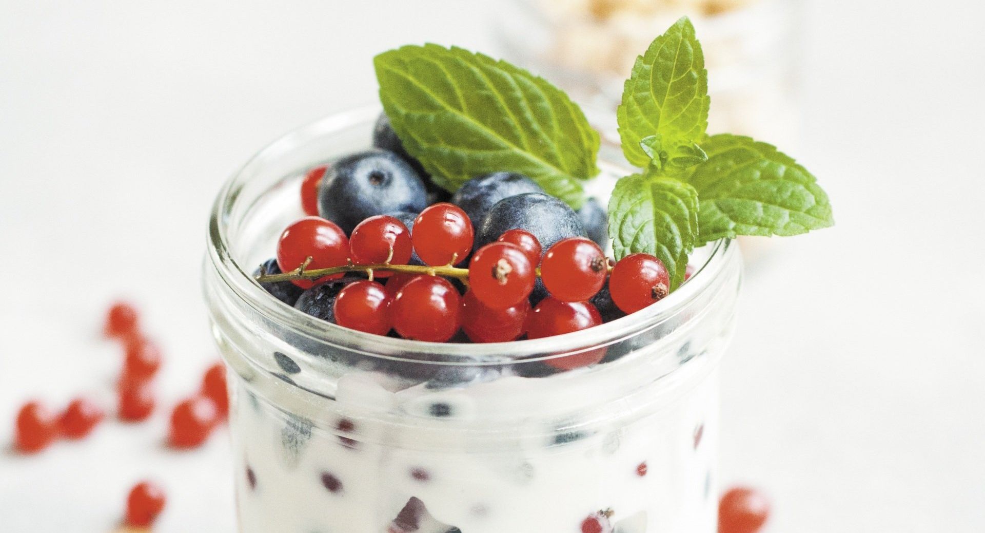 A jar of yogurt with blueberries and red currants on top.