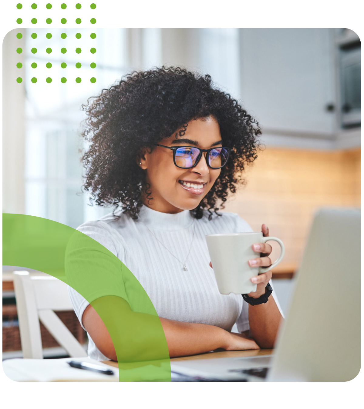 A woman is sitting at a table holding a cup of coffee and looking at a laptop.