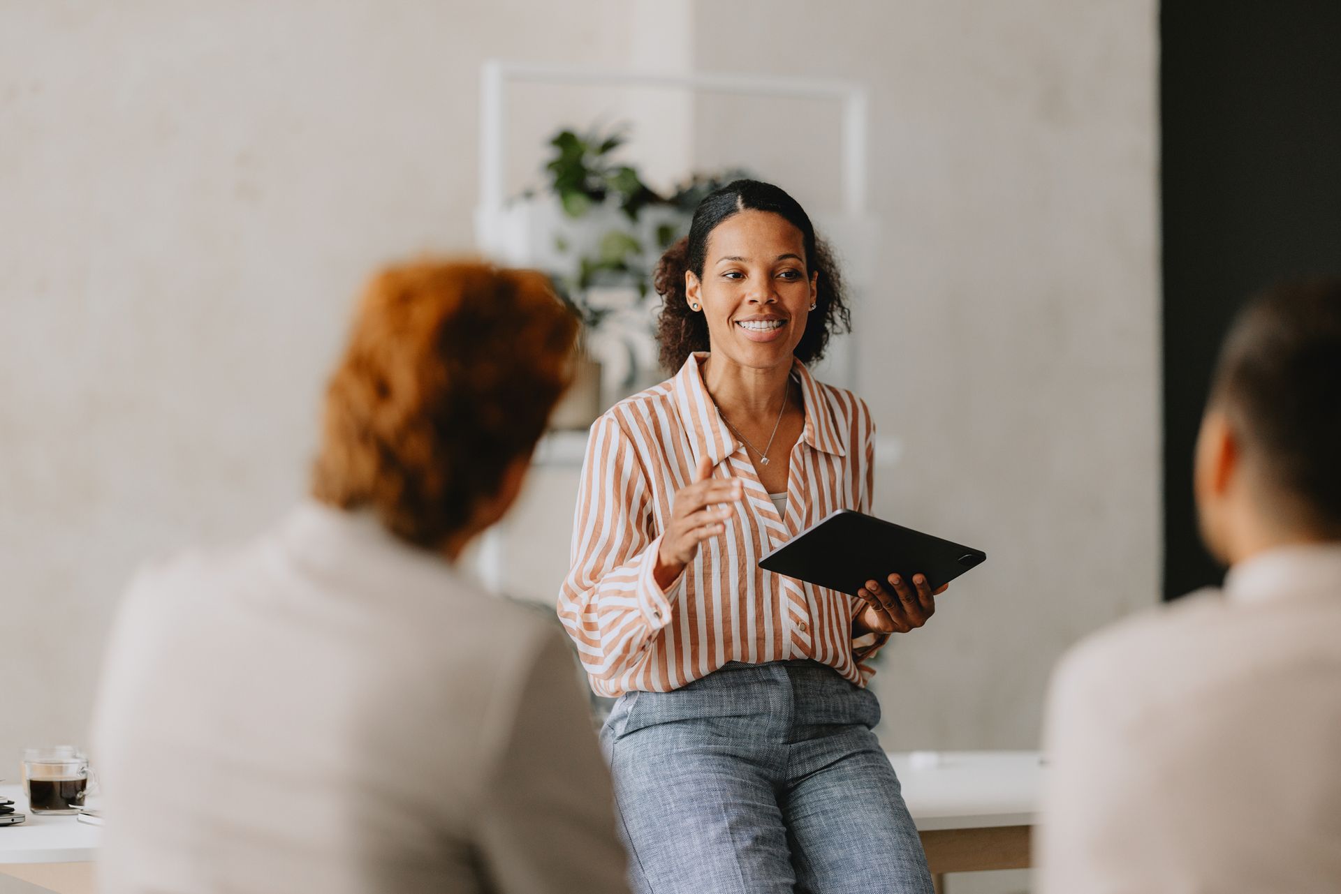 Woman with tablet gestures, smiling at two people in a meeting room.