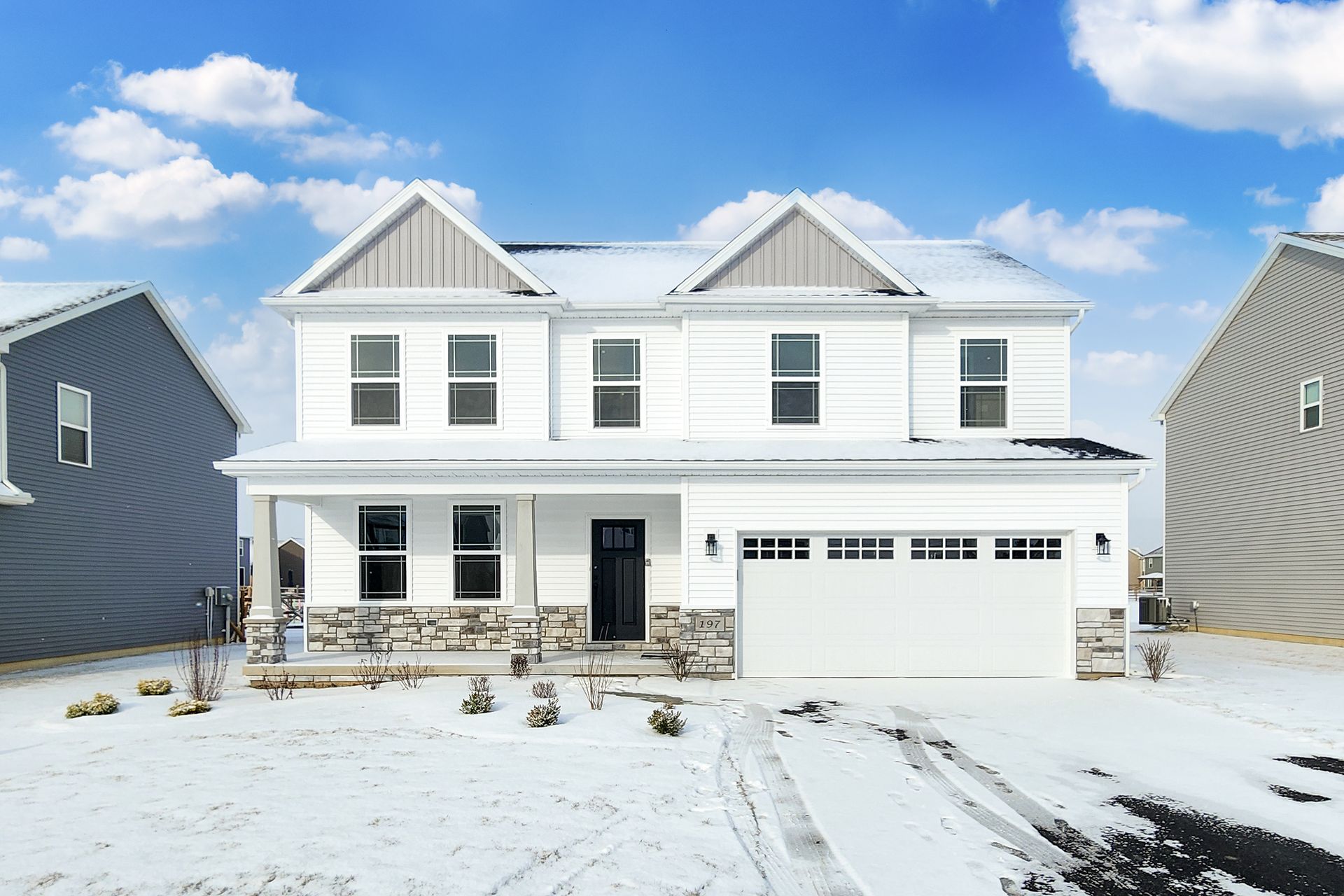 Two-story white house with snow-covered yard and cloudy sky; garage and stone accents.