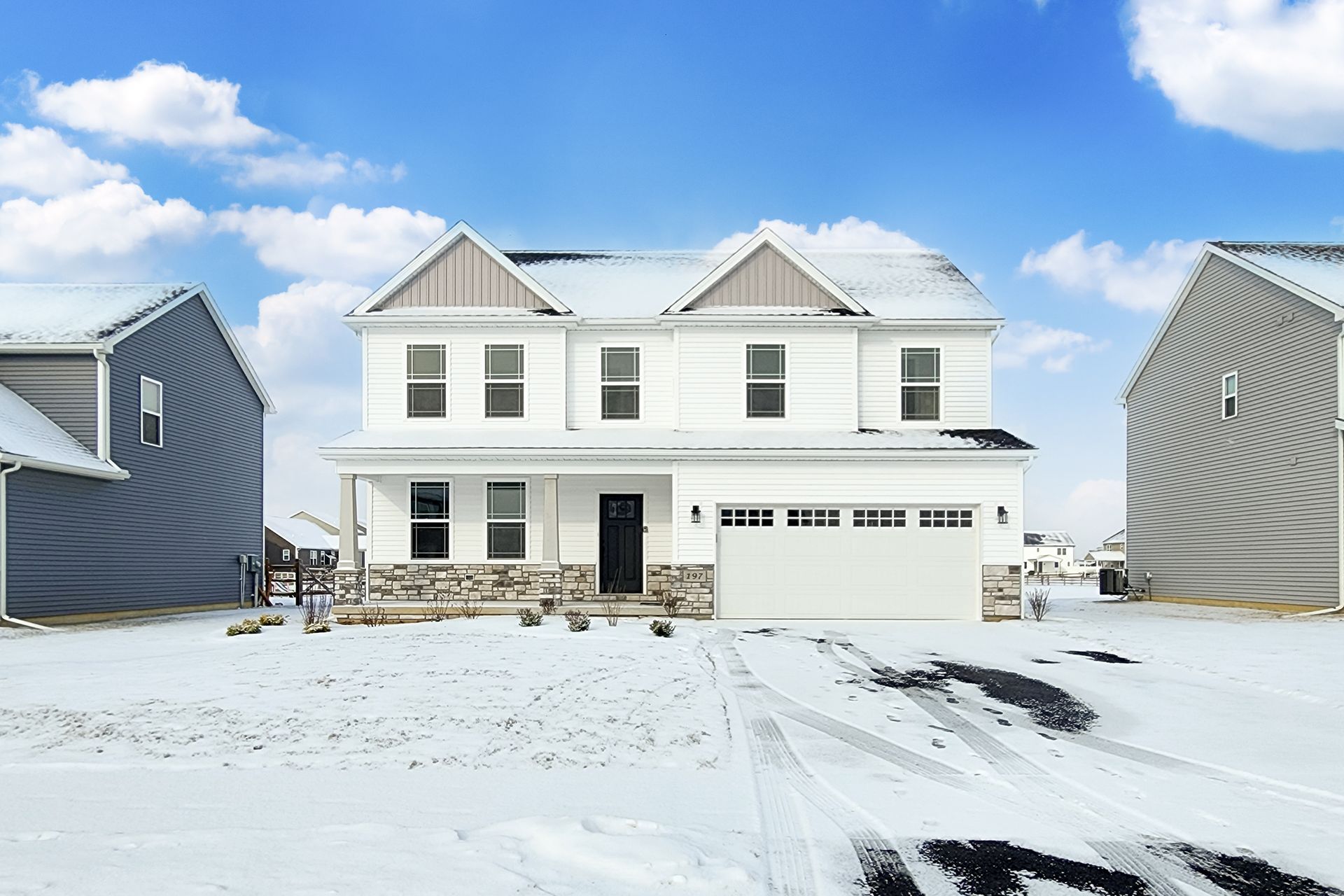 White two-story house with snow-covered lawn and clear blue sky. Garage and stone accents.