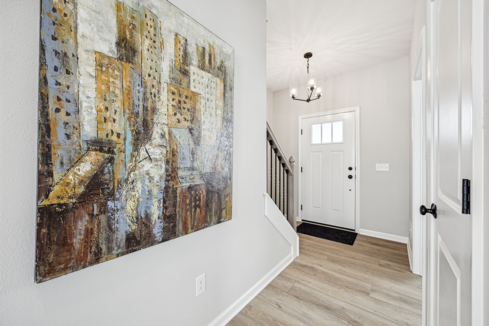 Hallway with abstract art, stairs, front door, and a chandelier.