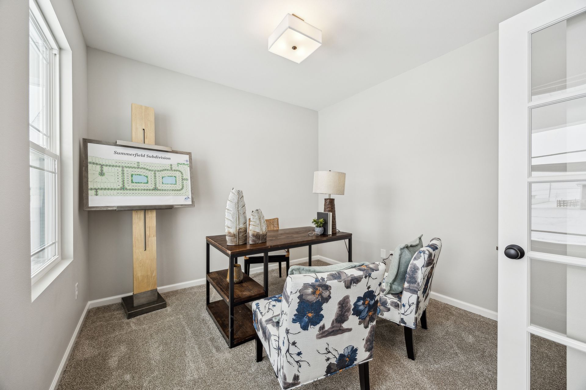 Home office with desk, two floral chairs, and architectural plans displayed on an easel.