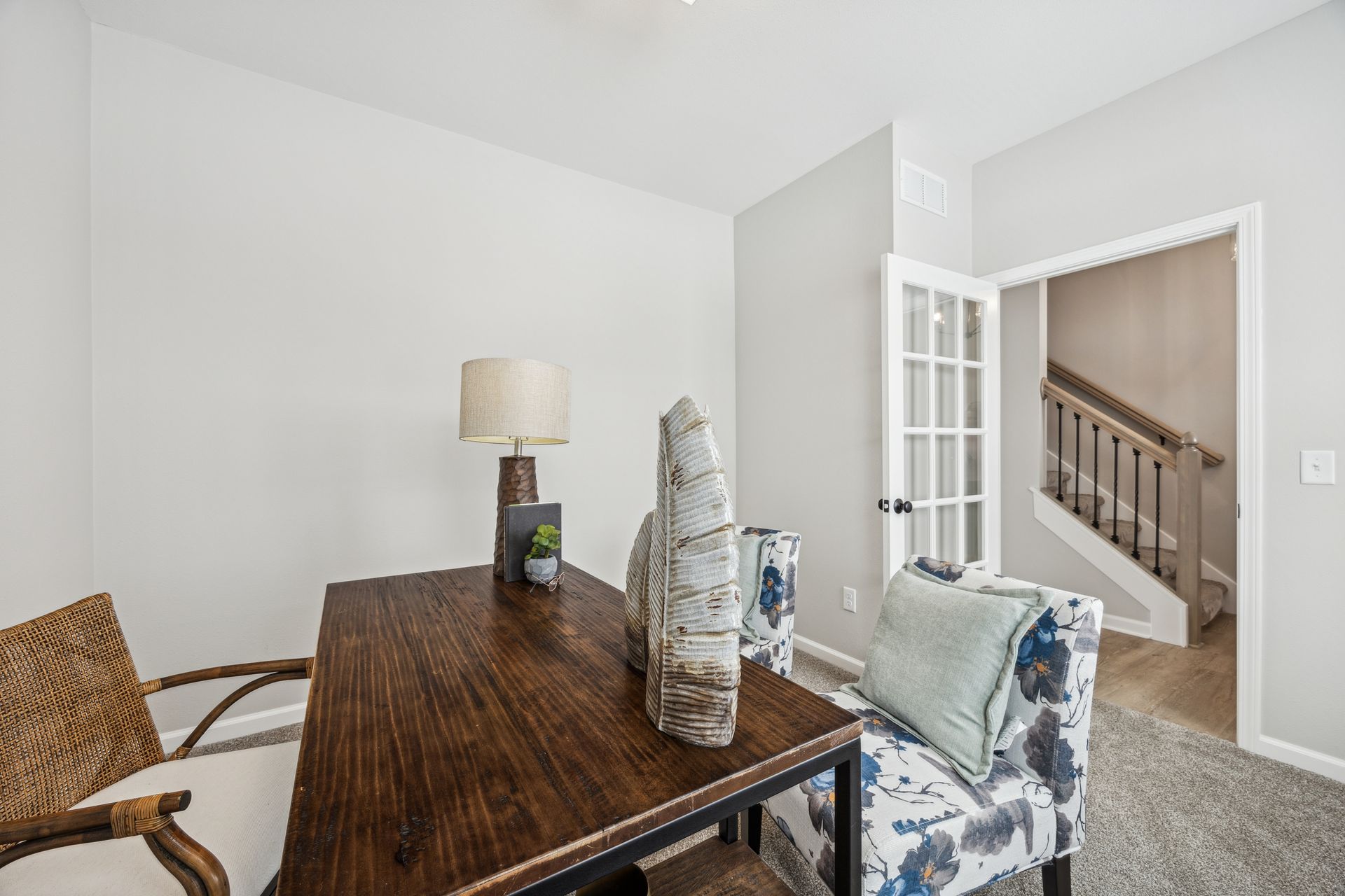 Home office with desk, chair, lamp, decorative items. French doors lead to a staircase.