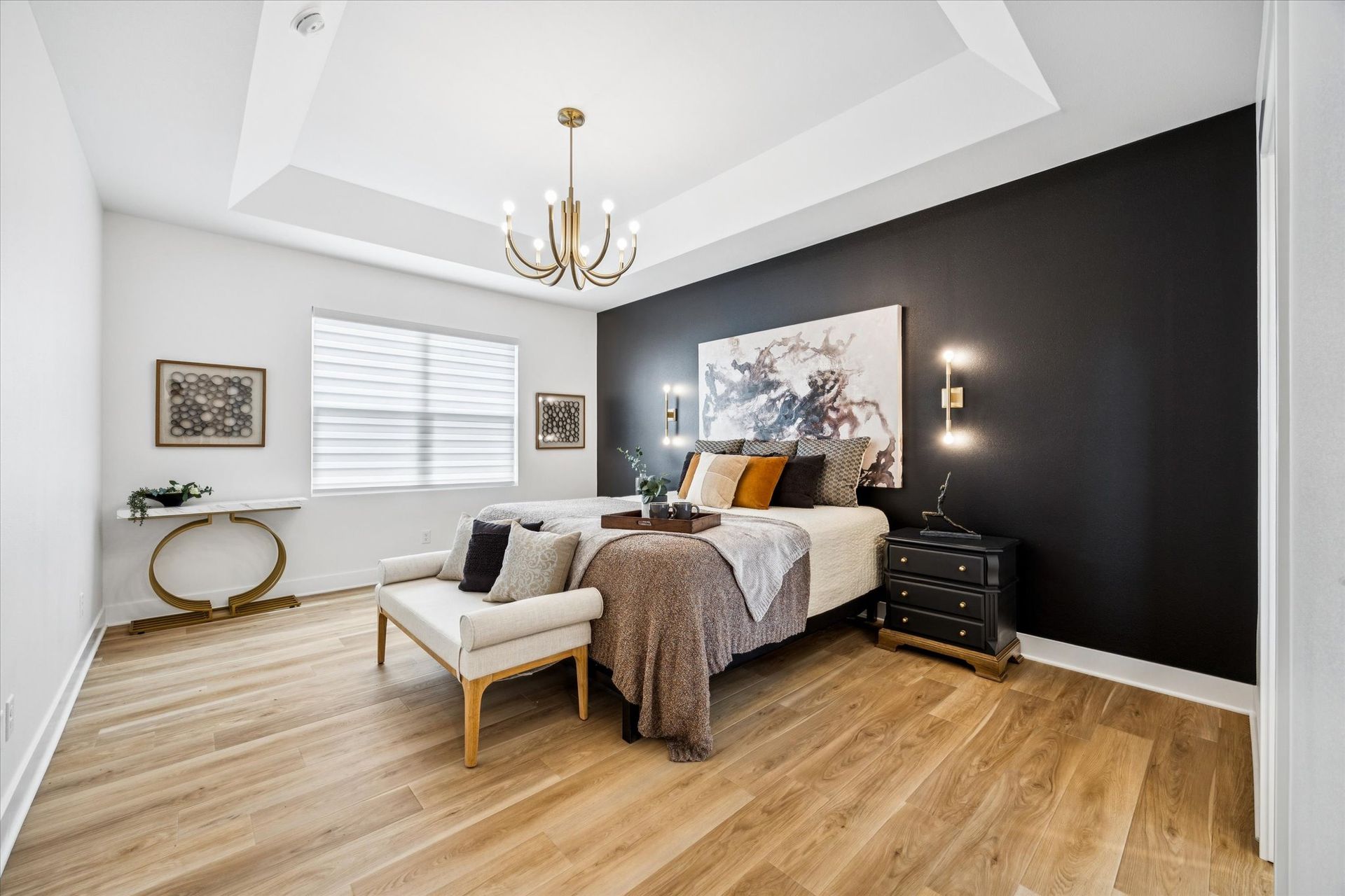 A bedroom with a bed , bench , nightstand and chandelier.