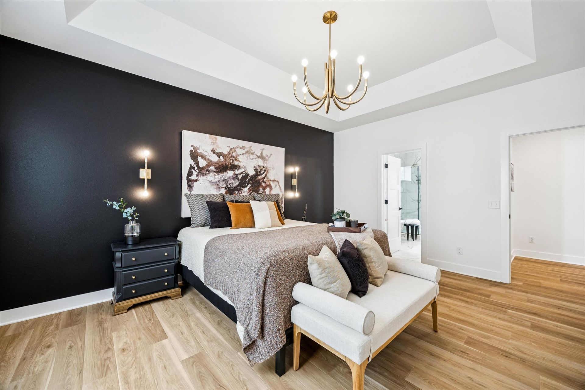 A bedroom with a bed , bench , nightstand and chandelier.