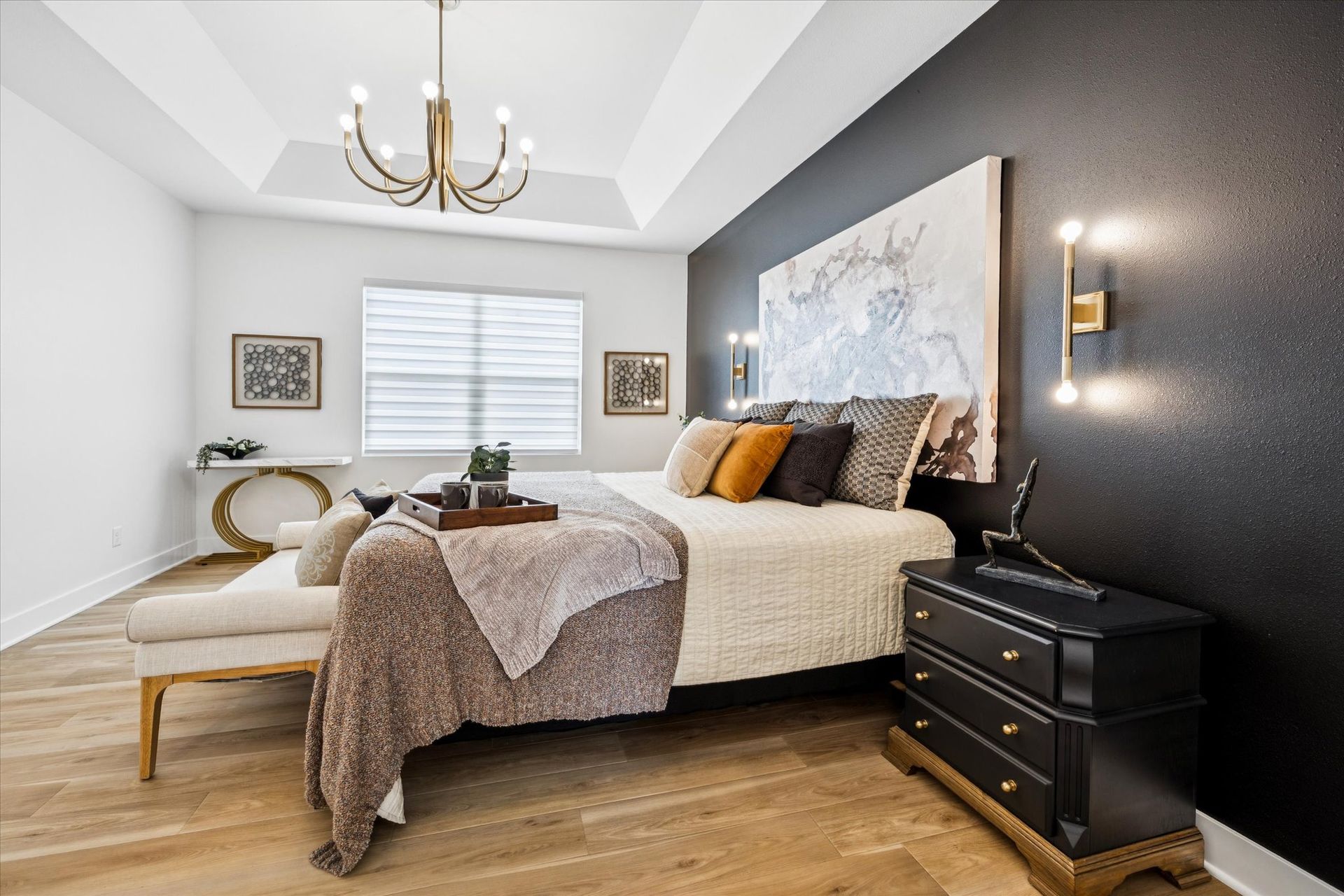 A bedroom with a large bed , dresser , bench and chandelier.