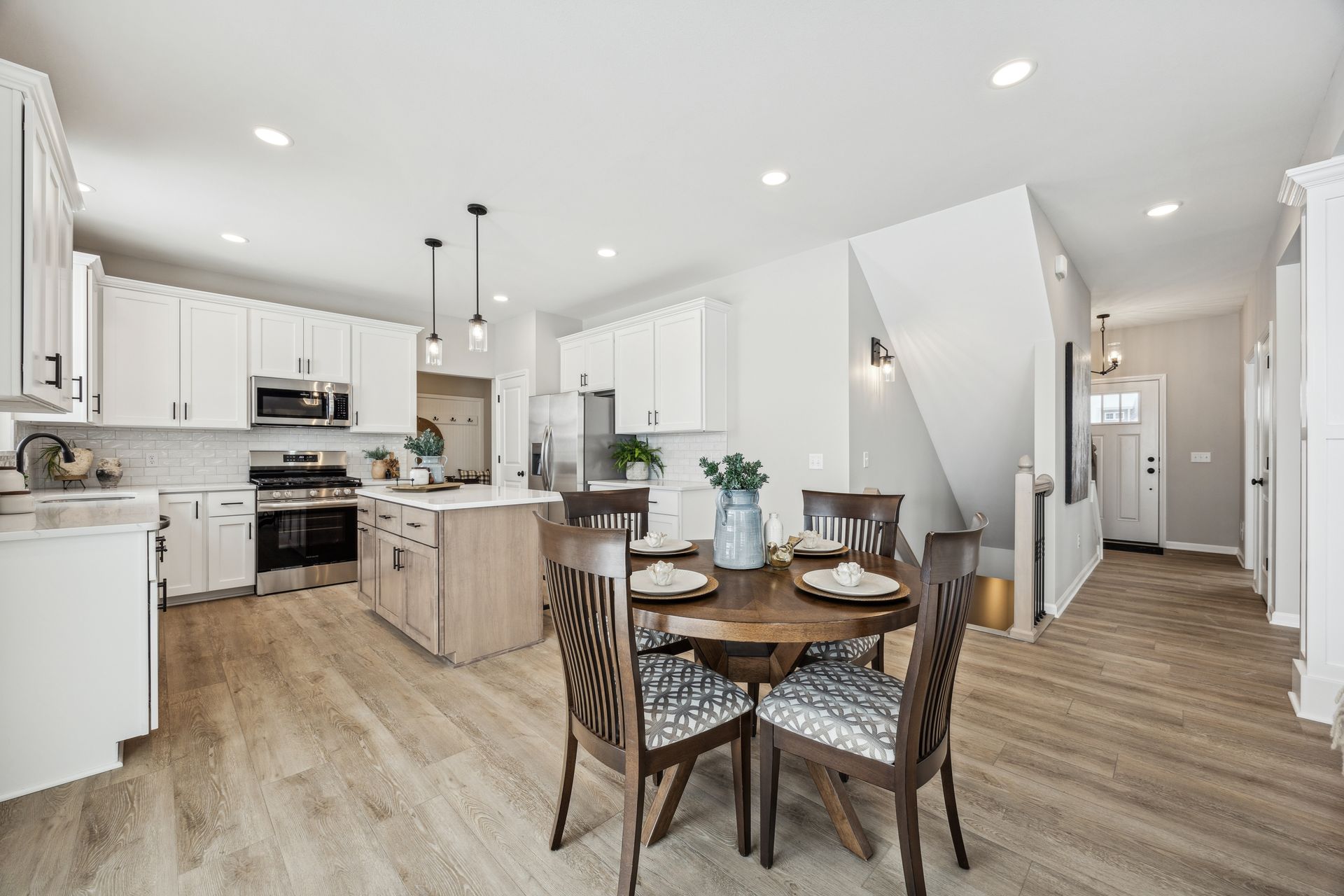 Open-concept kitchen and dining area with white cabinets, wood floors, and round table with four chairs.
