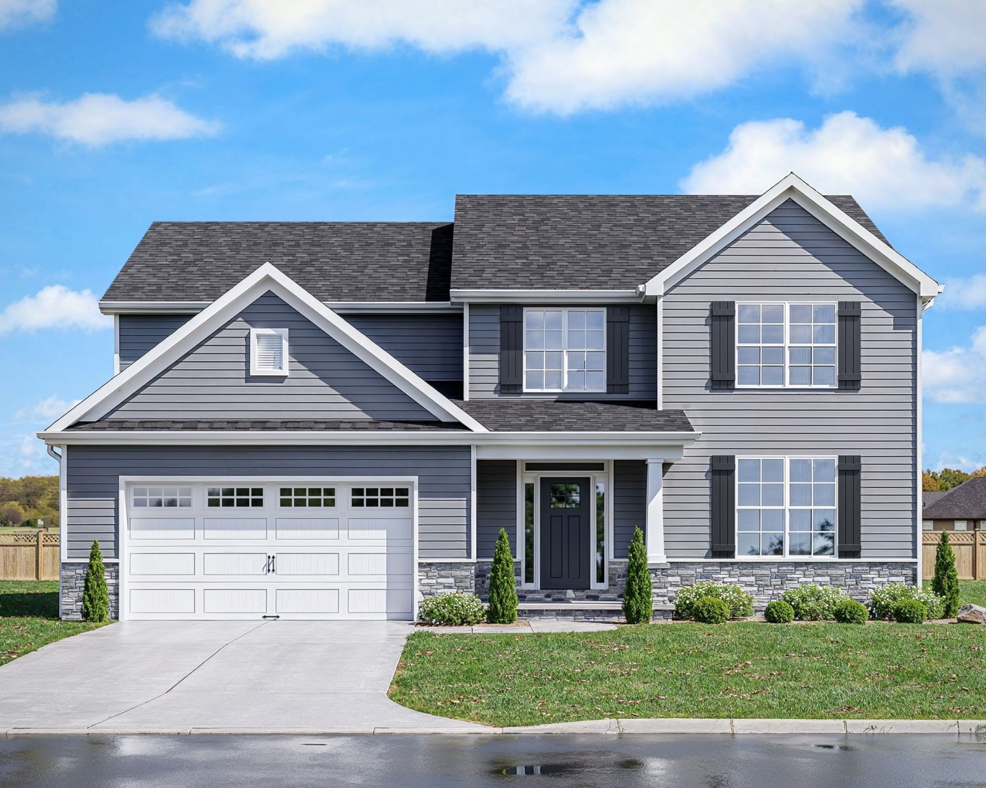 Two-story gray house with white garage door, black shutters, and stone accents, on a green lawn, under a blue sky.