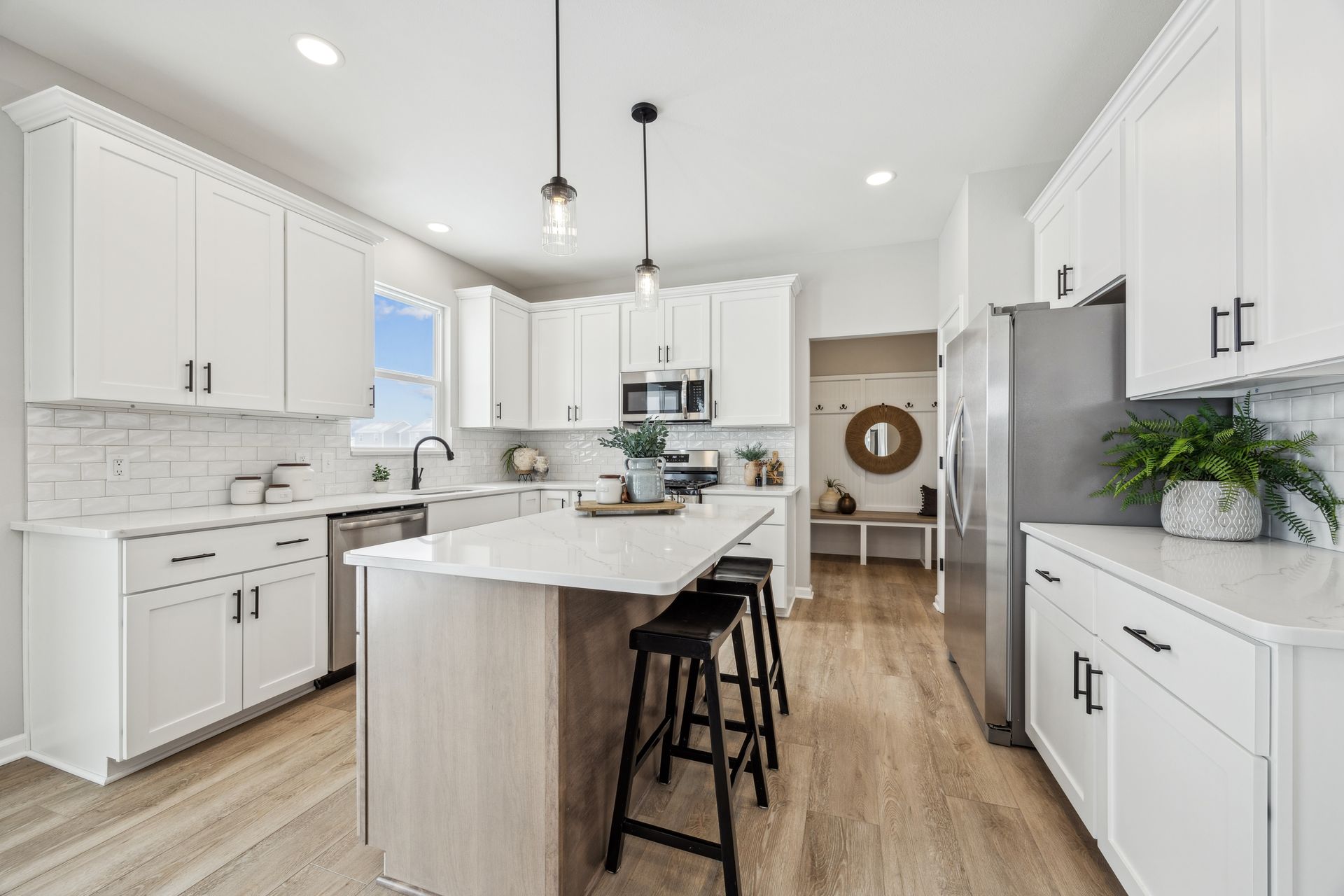 Modern white kitchen with island and black stools. Stainless steel appliances, light wood floors.