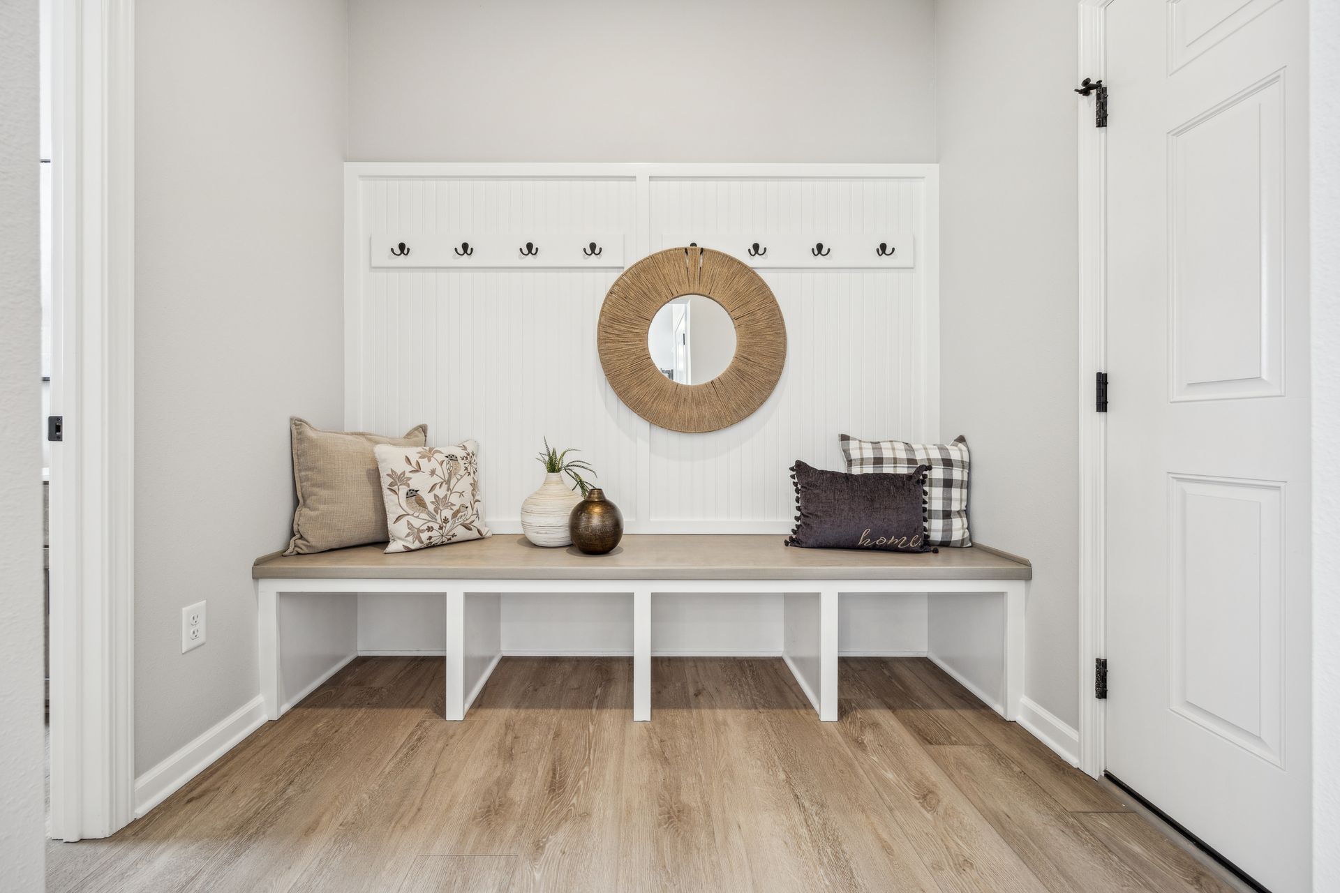 Entryway with a built-in bench, hooks, and a decorative wreath, featuring pillows and vases.