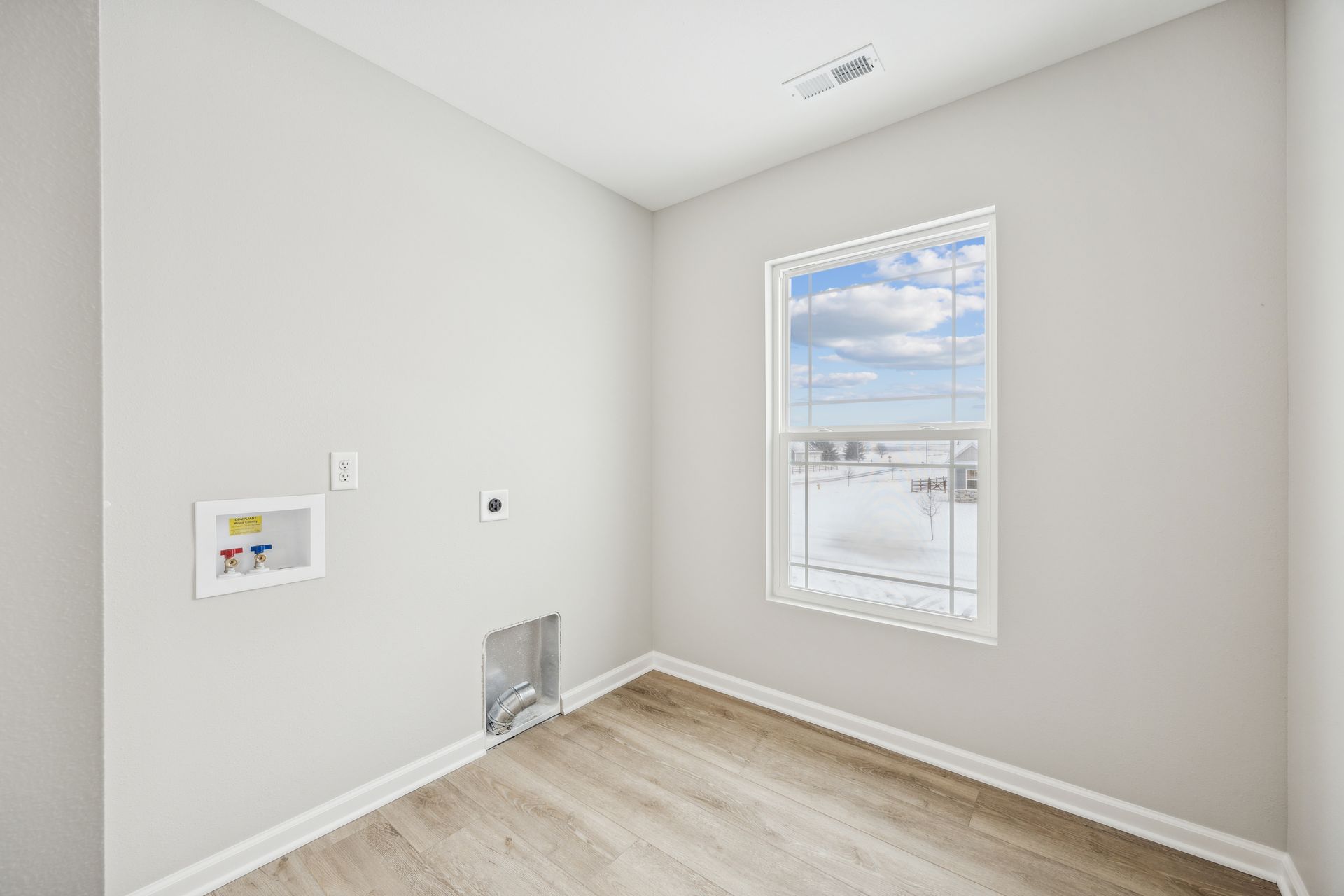 Laundry room with window, utility hookups, and light wood-look flooring, painted walls.