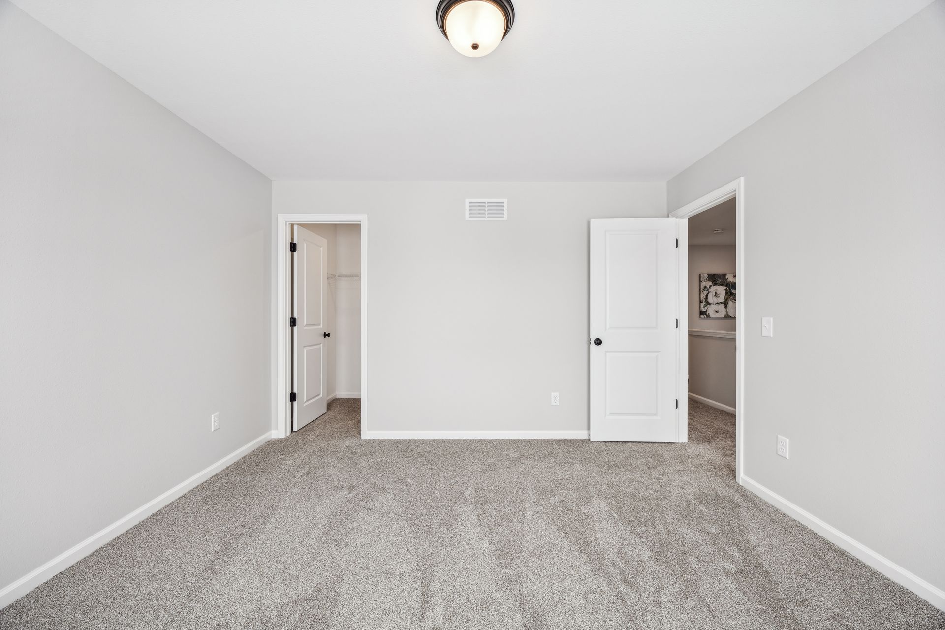 Empty bedroom with gray carpet, gray walls, two white doors, and a closet.