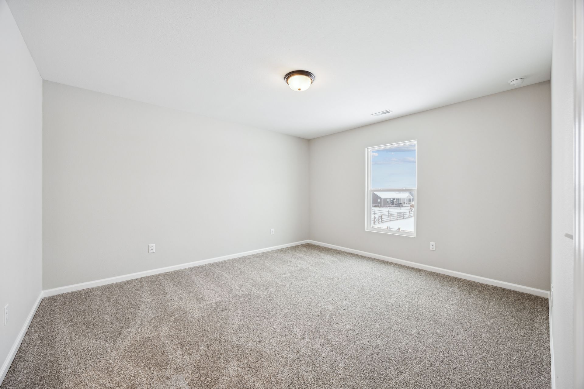 Empty bedroom with gray carpet, walls, and a window with a snowy view.