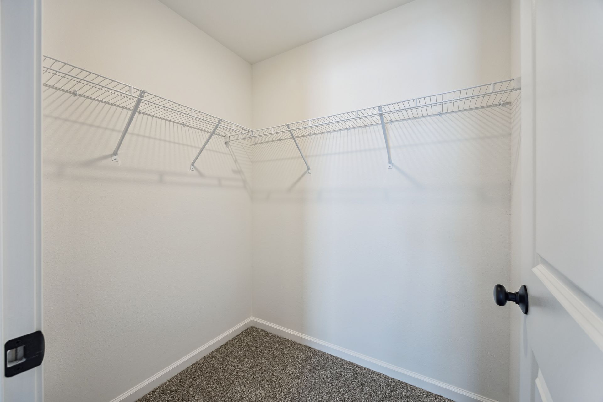 Empty white closet with wire shelving and gray carpet. Open door on right.