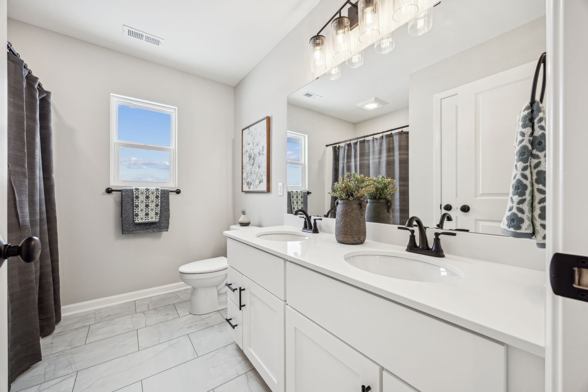 Bright bathroom with white vanity, double sinks, and black fixtures.