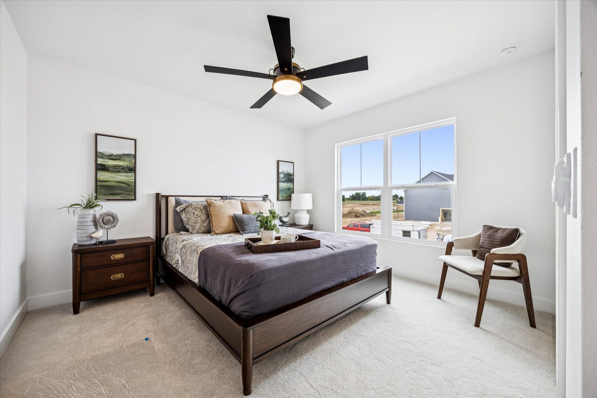 A bedroom with a bed , nightstand , chair and ceiling fan.