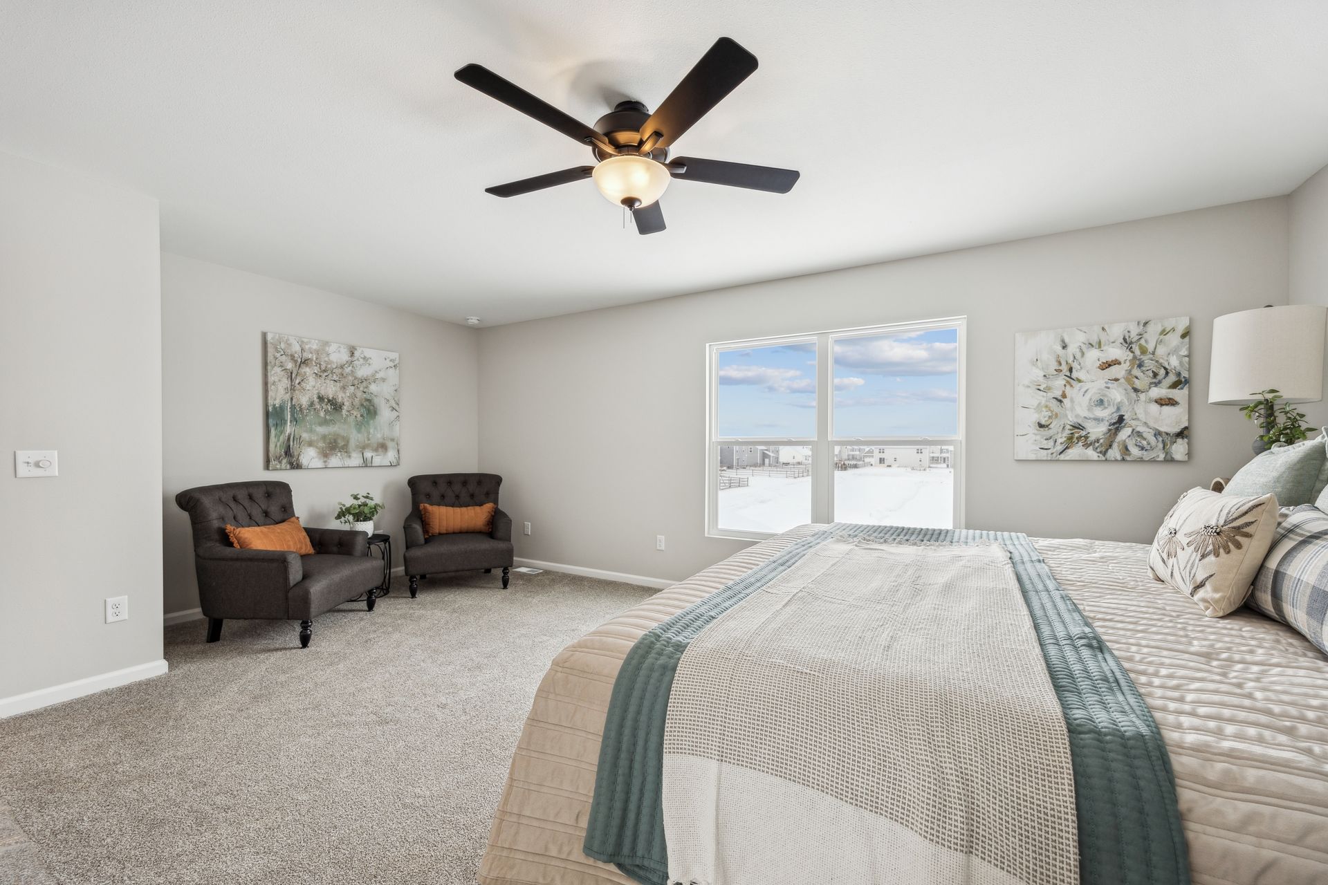 Bedroom with a large bed, two armchairs, artwork, and a ceiling fan.