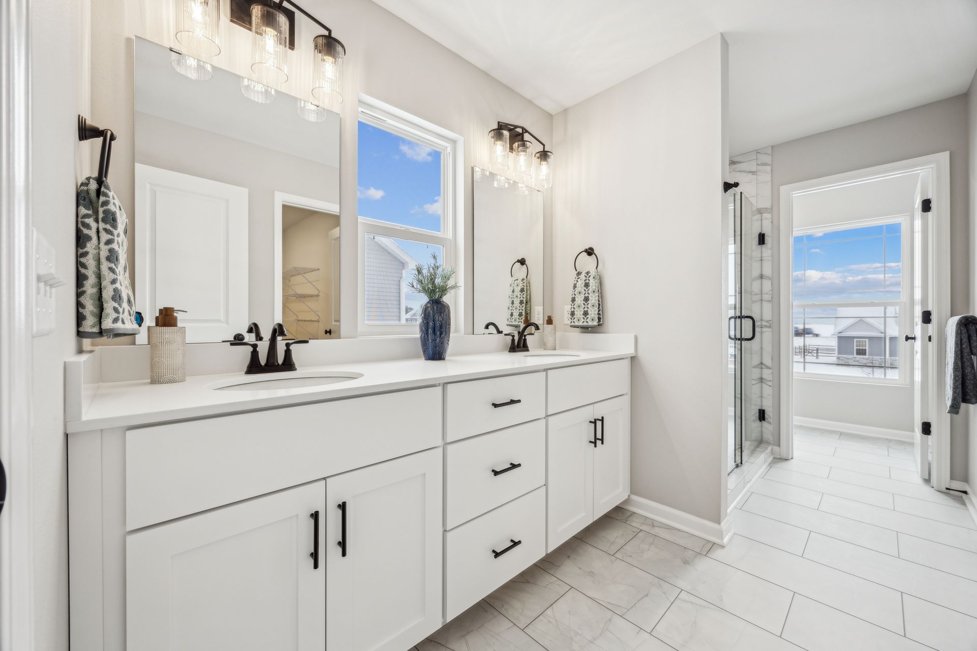 Bright, white bathroom with double vanity, large mirrors, and shower entrance.