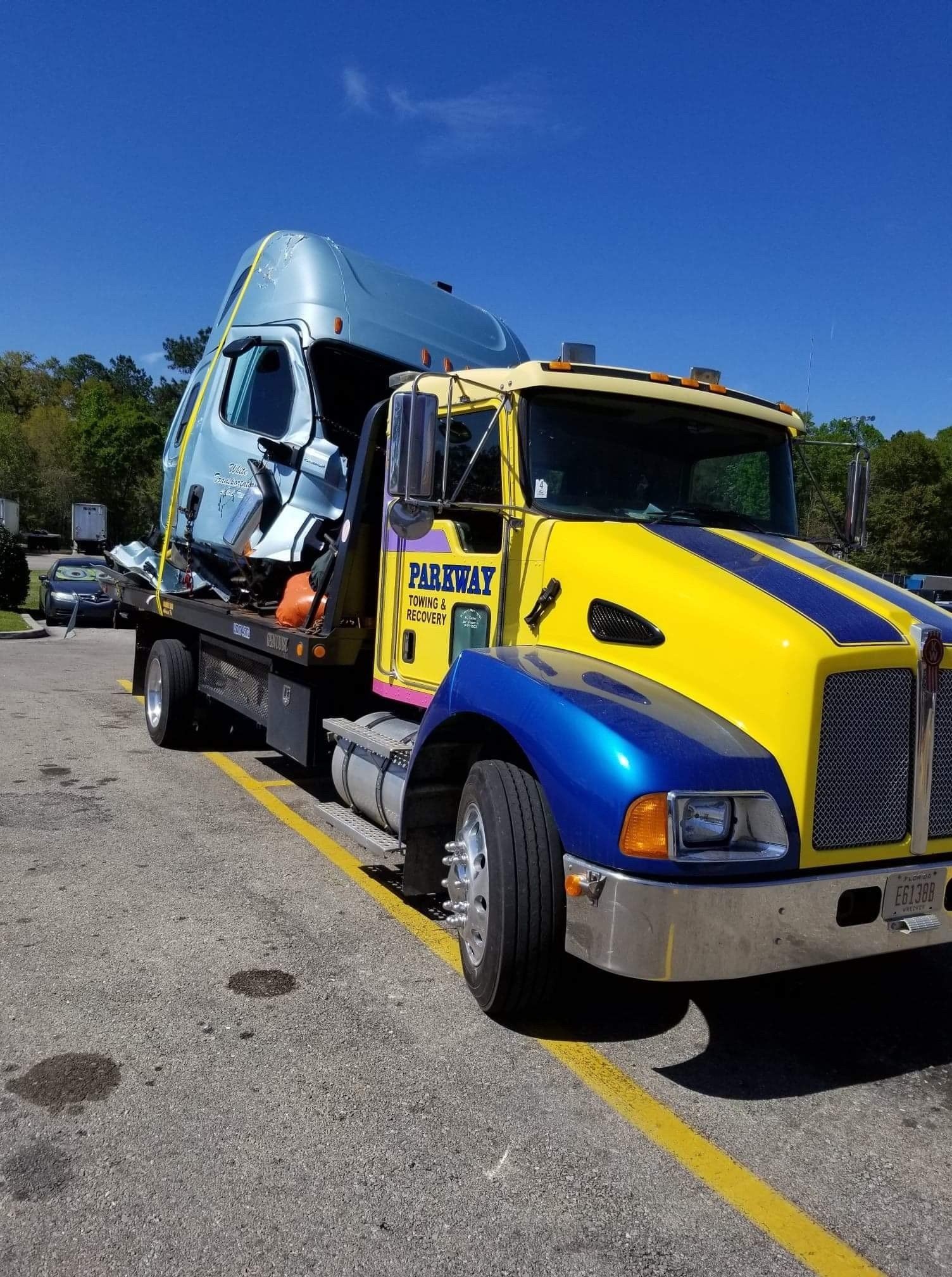 Bright yellow tow truck hauling a blue semi truck cab on a sunny roadside