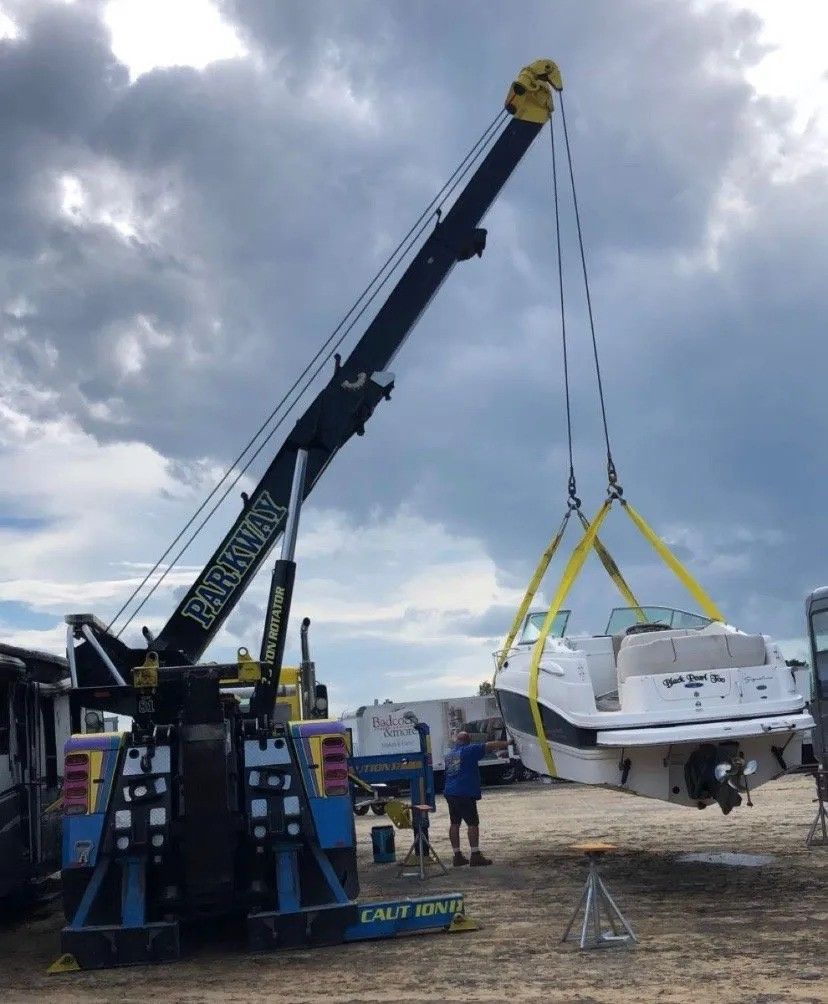 Crane lifting a white boat at a dock under cloudy skies, with workers nearby