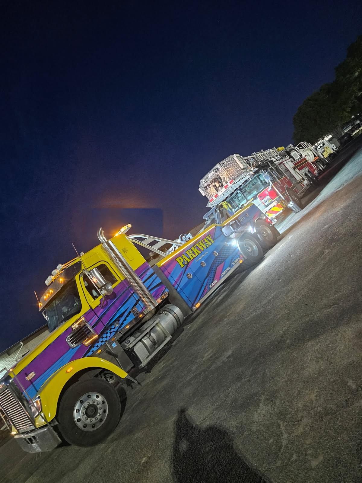 Colorful tow truck at night on a road, angled with bright lights and a dark sky.