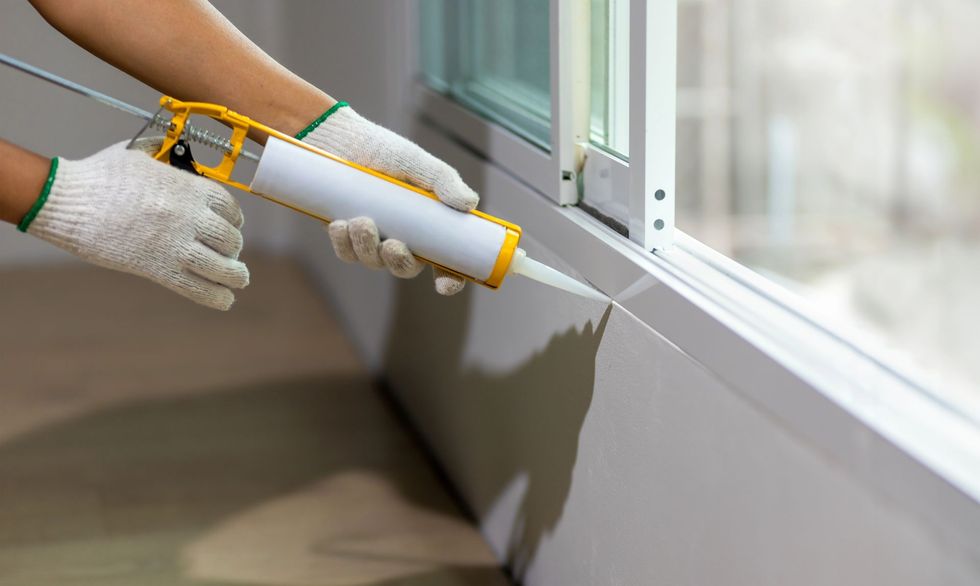 Persona che sigilla il telaio di una finestra con una pistola per sigillante, indossando i guanti.