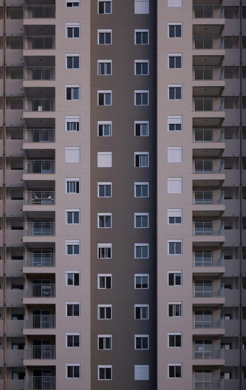 Facciata di un alto condominio con balconi e numerose finestre. Sezioni grigio chiaro e scuro.