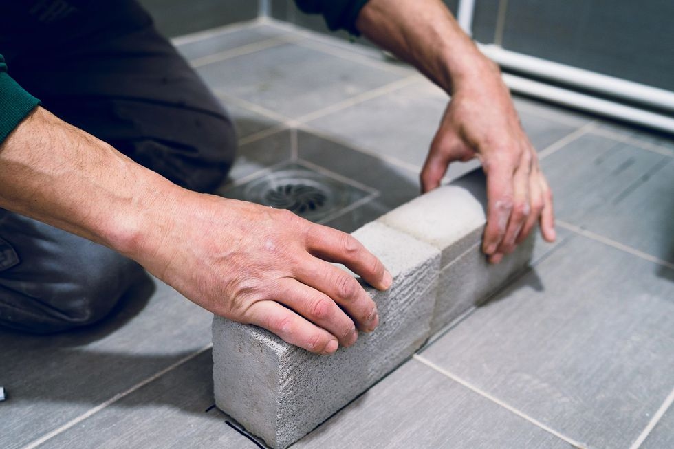 Persona che posiziona un mattone di piastrelle grigie in un bagno con pavimento in piastrelle grigie.