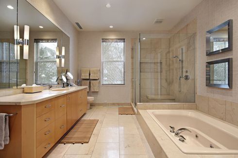 Bagno luminoso con lungo mobile lavabo in legno, doccia in vetro, vasca da bagno, due specchi e una finestra.