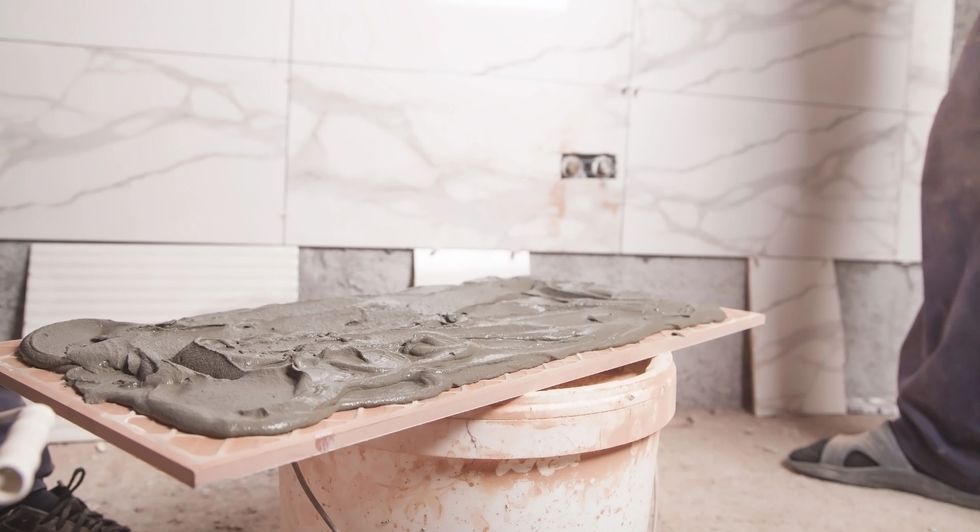 Piastrelle posate con malta su una tavola di legno, su un secchio, in un bagno in costruzione.