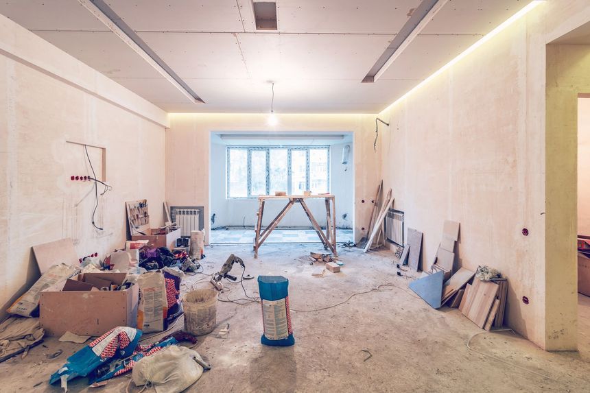 Stanza in fase di ristrutturazione con detriti sul pavimento, cartongesso e soffitto parzialmente rifinito.