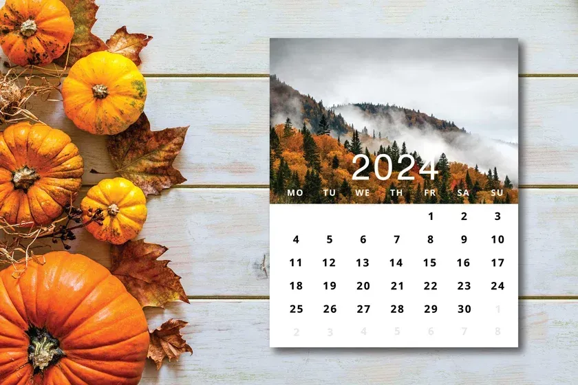 Un calendrier pour l'année 2024 est entouré de citrouilles et de feuilles sur une table en bois.