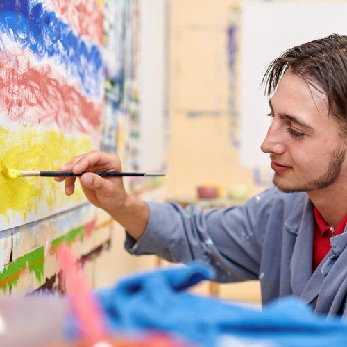 Jugendlicher malt ein Streifenbild in gelb, blau und rot