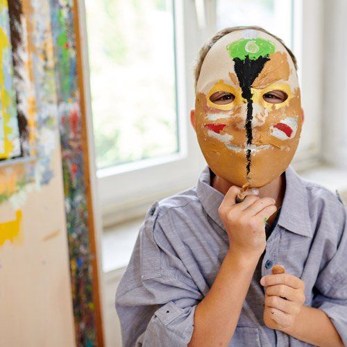 Junge hält eine bemalte Maske vor sein Gesicht