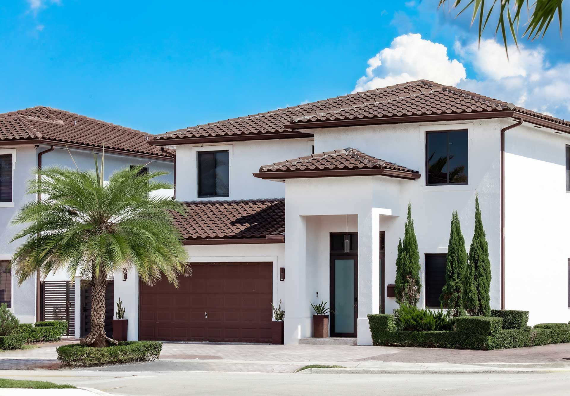 white painted Spanish style home with tile roof and palm tree in front