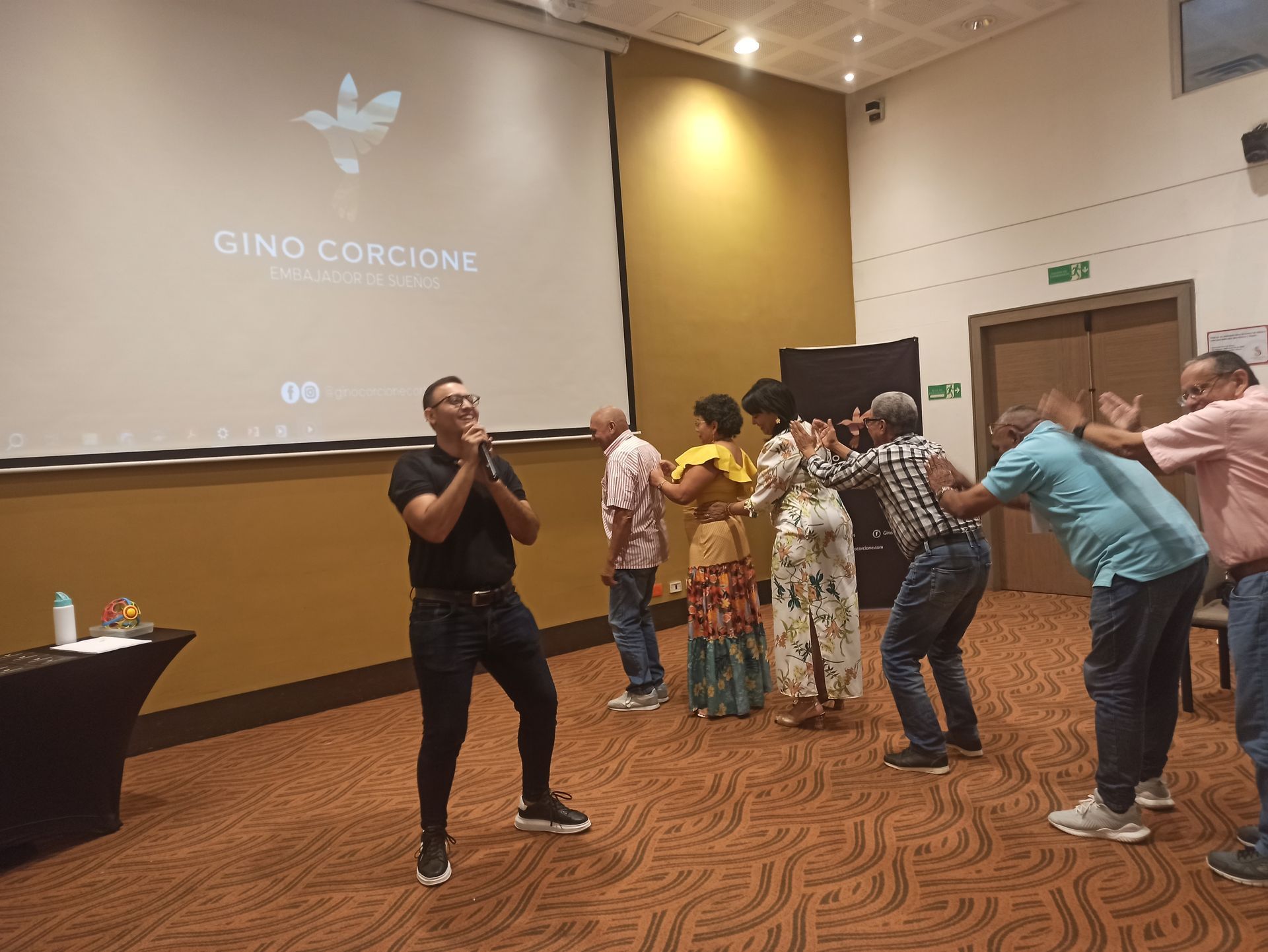 Un grupo de personas está bailando en una habitación frente a una pantalla grande.