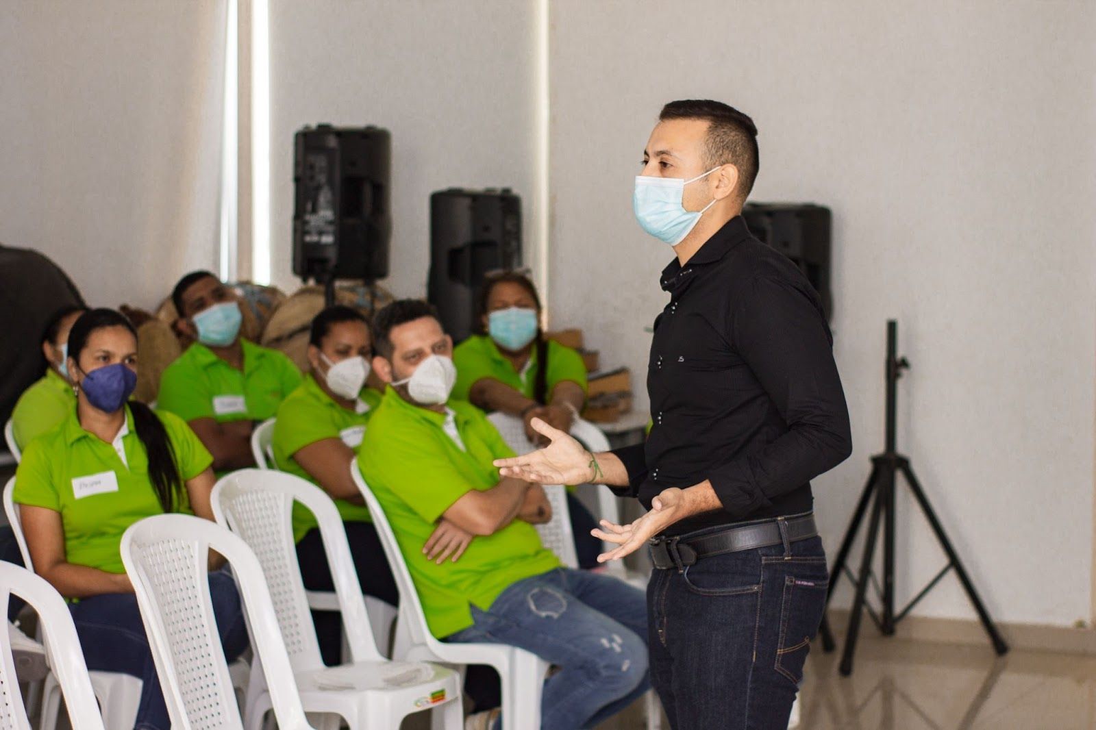 Un hombre que lleva una máscara está hablando con un grupo de personas sentadas en sillas.