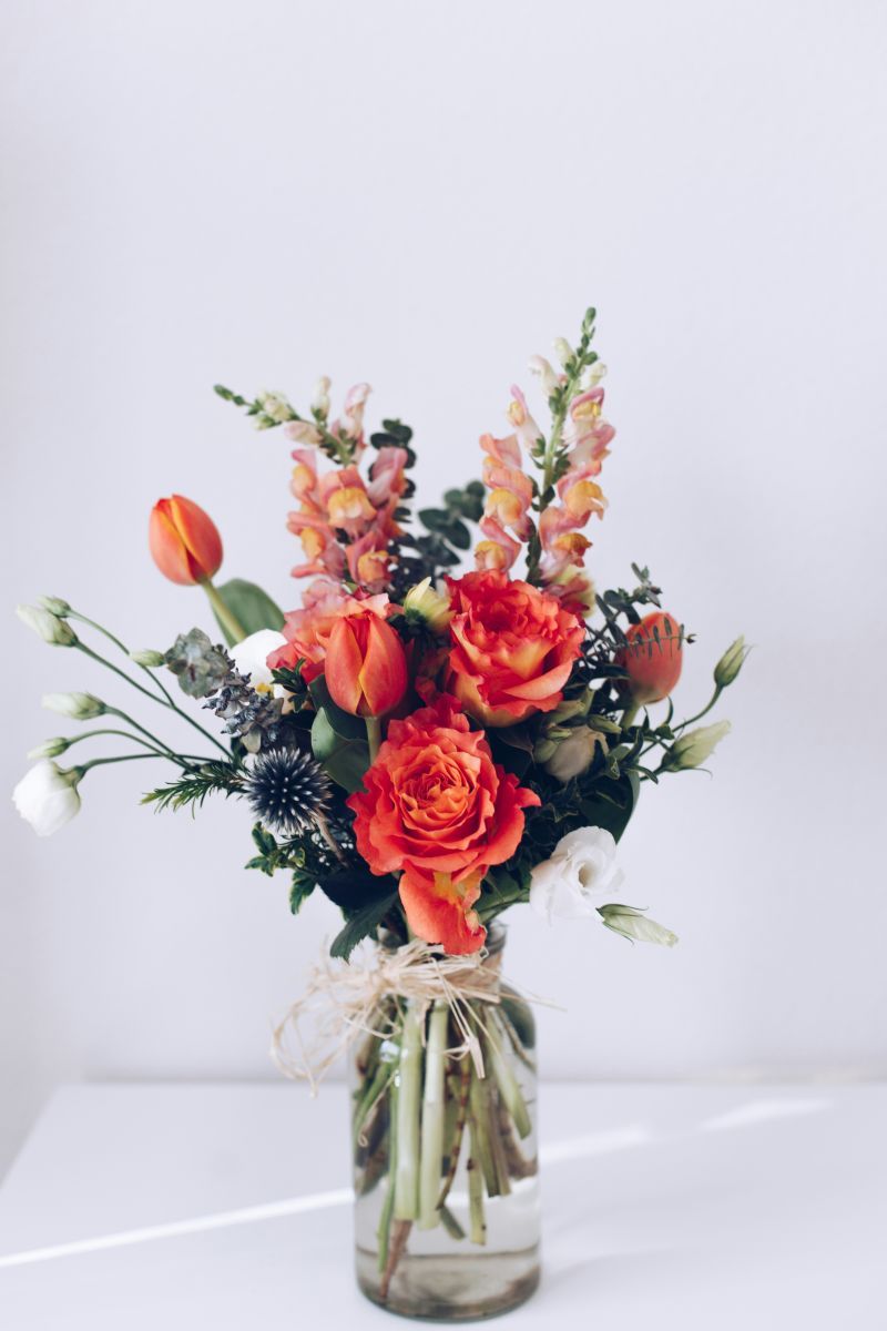 Orange and red floral arrangement in a clear glass vase on a white background