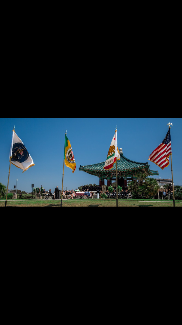 Four flags fly in a row before a traditional Korean pavilion set against a bright blue sky.