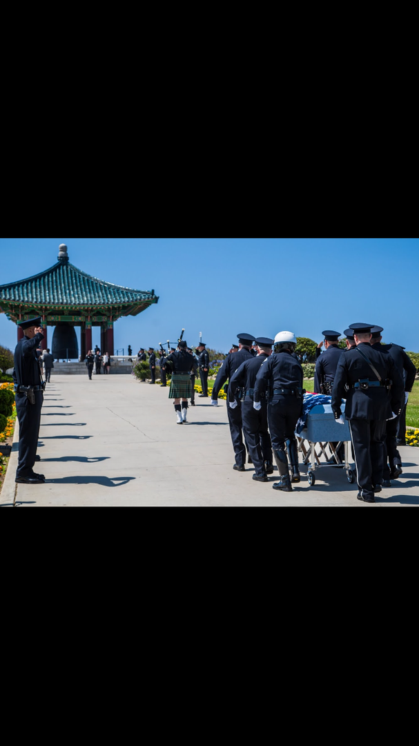 A bagpiper leads a procession of police officers carrying a flag-draped casket toward the Korean Bell of Friendship.