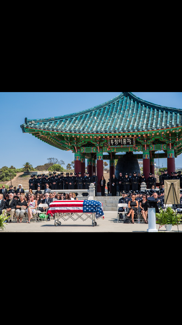 A funeral service with a flag-draped casket held in front of the Korean Bell of Friendship in San Pedro, California.
