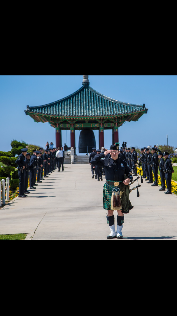 A bagpiper in uniform leads a column of saluting officers toward the Korean Bell of Friendship in San Pedro, California.