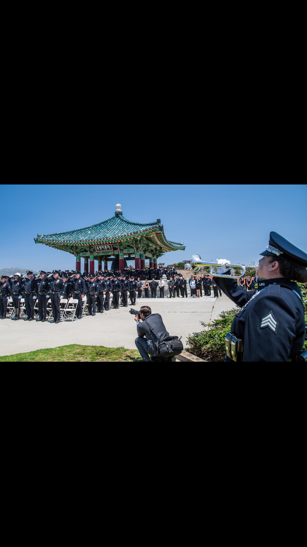 A photographer crouches to capture a formation of uniformed personnel near an ornate, traditional East Asian-style pavilion.